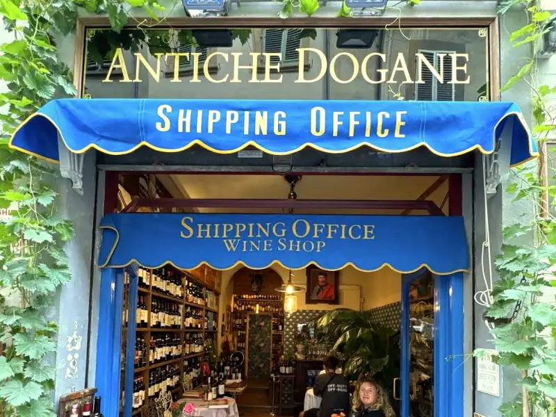 The Antiche Dogane shop front in Florence, with its blue Shipping Office awning and the wine shop visible through the doorway